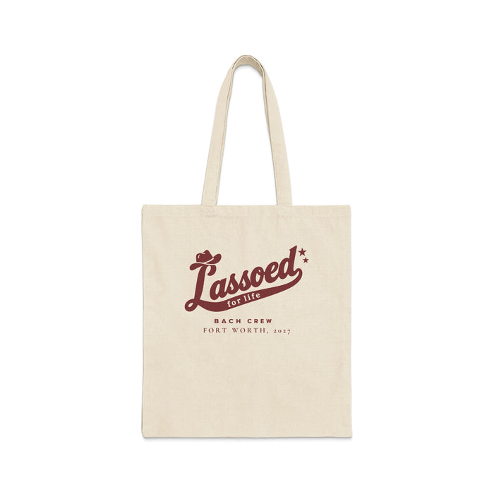 A beige canvas tote bag features brown text reading "Lassoed for life Bach Crew Fort Worth, 2027".