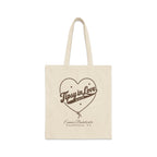 A plain canvas tote bag featuring brown print with a rope-outlined heart, stars, and text reading Tipsy in Love Bach.