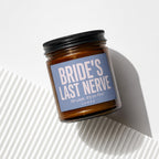 Amber glass candle with blue label reading "BRIDE'S LAST NERVE Oh Look, It's on Fire!"