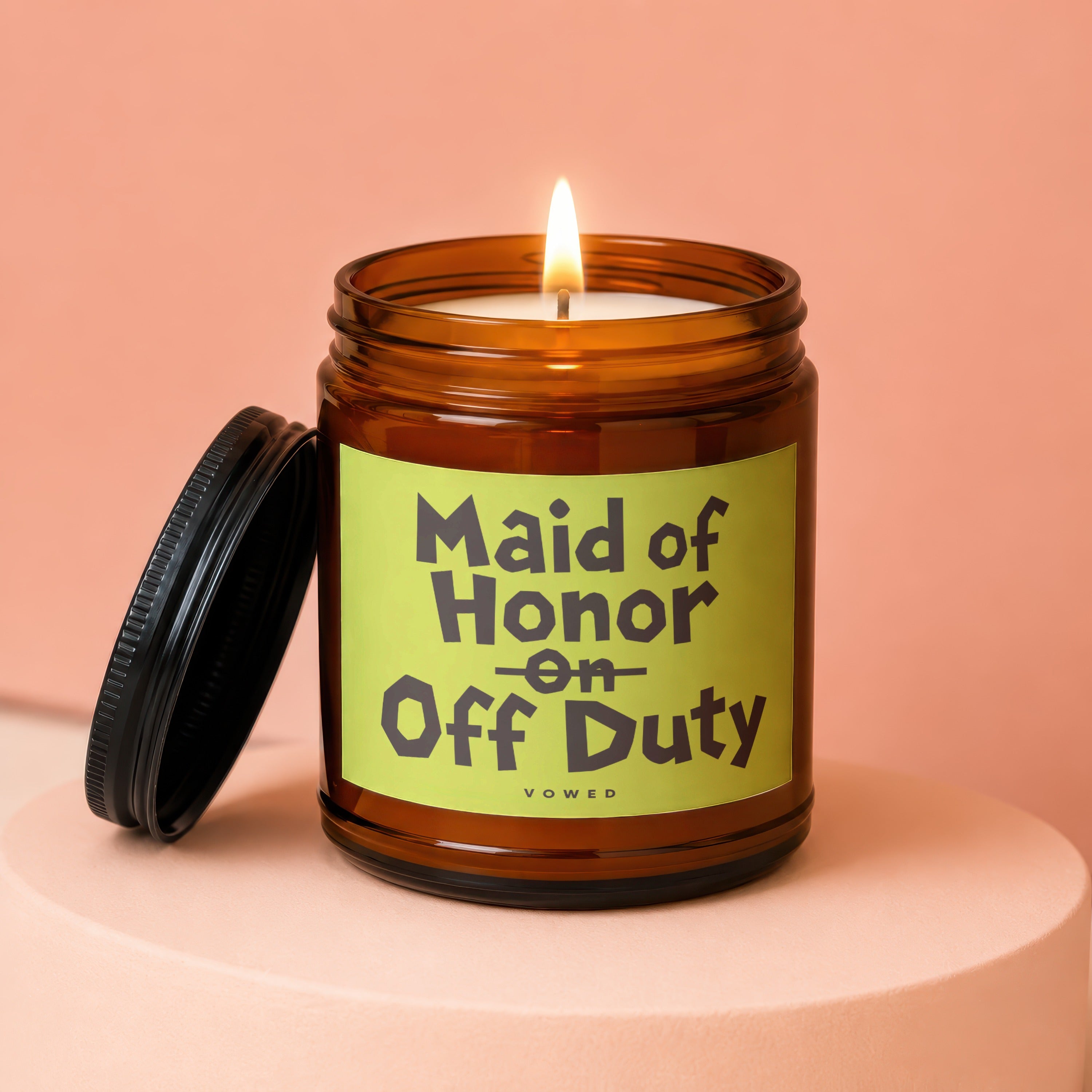 Amber jar candle with lit wick and lid off, reads "Maid of Honor Off Duty".