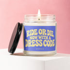 Glass candle with lit wick labeled "RIDE OR DIE, NOW WITH A DRESS CODE".