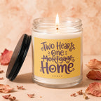 Lit glass jar candle with yellow label reading "Two Hearts, One Mortgage Home".