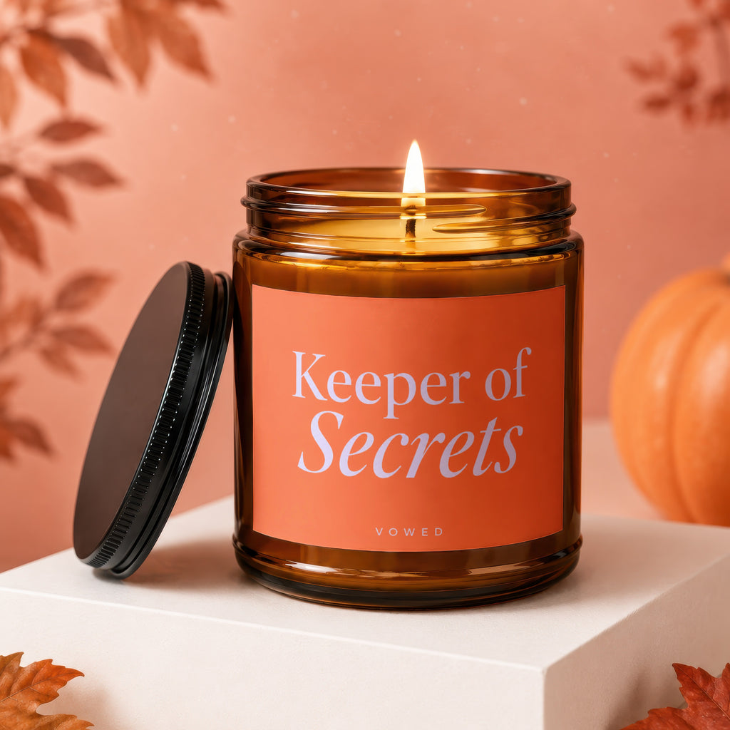 Amber jar candle with lit flame, orange label reads "Keeper of Secrets."
