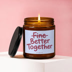 Amber glass candle with lid off, burning, reads "Fine Better Together VOWED".