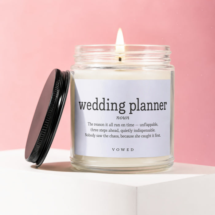 Candle with "wedding planner noun" and quote on white label, black lid beside it.