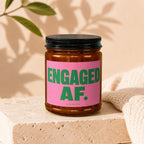 Candle jar with black lid, pink label reads "ENGAGED AF. VOWED".