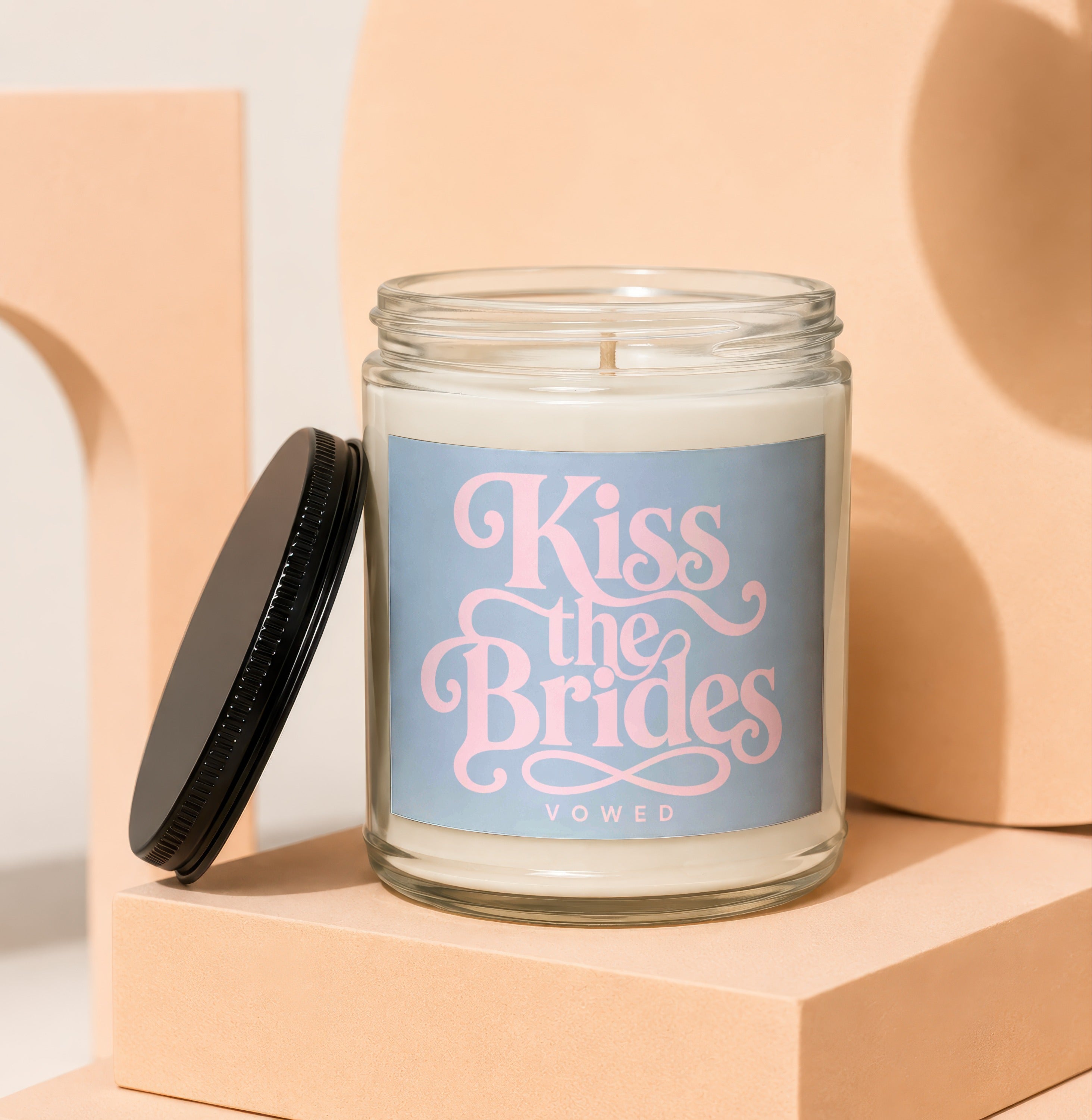 Glass candle with pink "Kiss the Brides" text and "VOWED" on a blue label.
