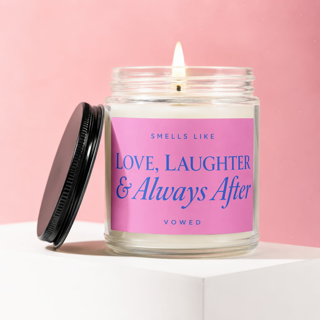 Lit candle in glass jar with pink label reading "Smells Like Love, Laughter & Always After Vowed".