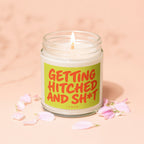 Glass jar candle with lit wick, labeled "GETTING HITCHED AND SH\*T" by VOWED.