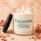 Scented candle labeled "Engagement Bliss" on a peachy background with dried leaves.