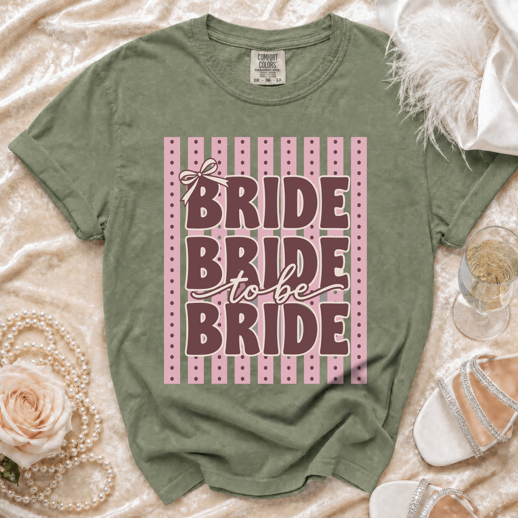 Green t-shirt with "BRIDE to be BRIDE" text on pink and green striped background.