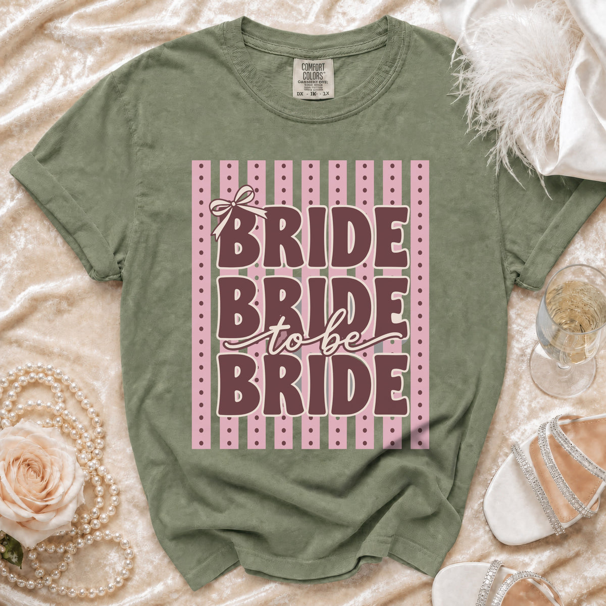 Green t-shirt with "BRIDE to be BRIDE" text on pink and green striped background.