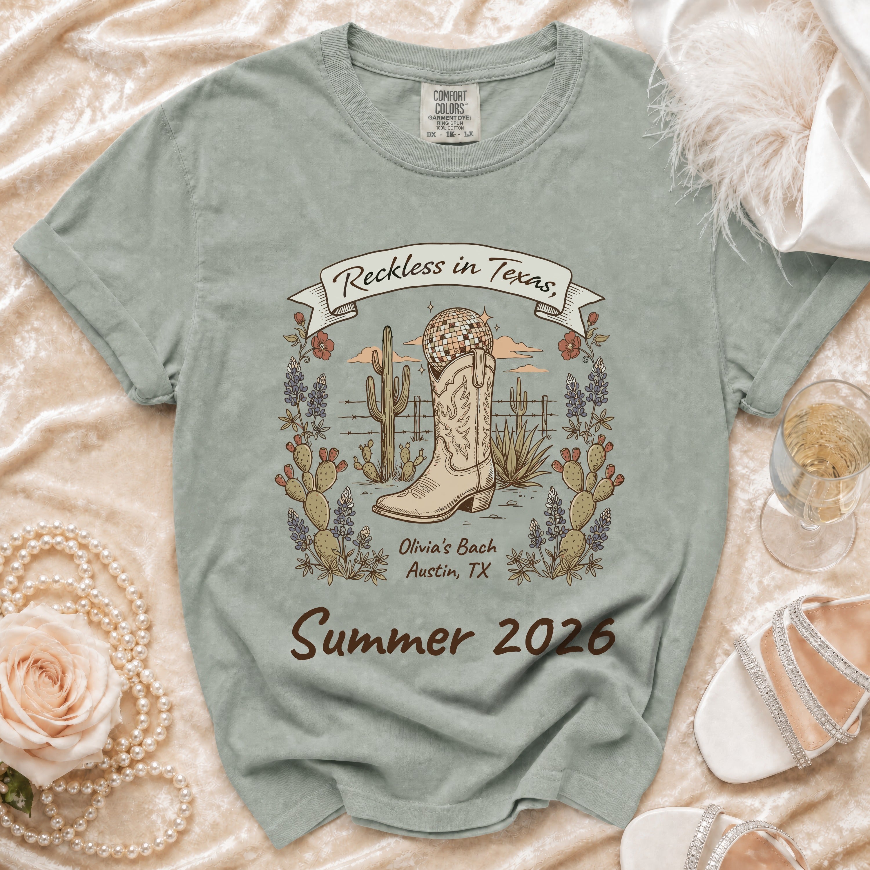 T-shirt graphic with cowboy boot, disco ball, cacti, and text "Reckless in Texas, Olivia's Bach Austin, TX Summer 2026".