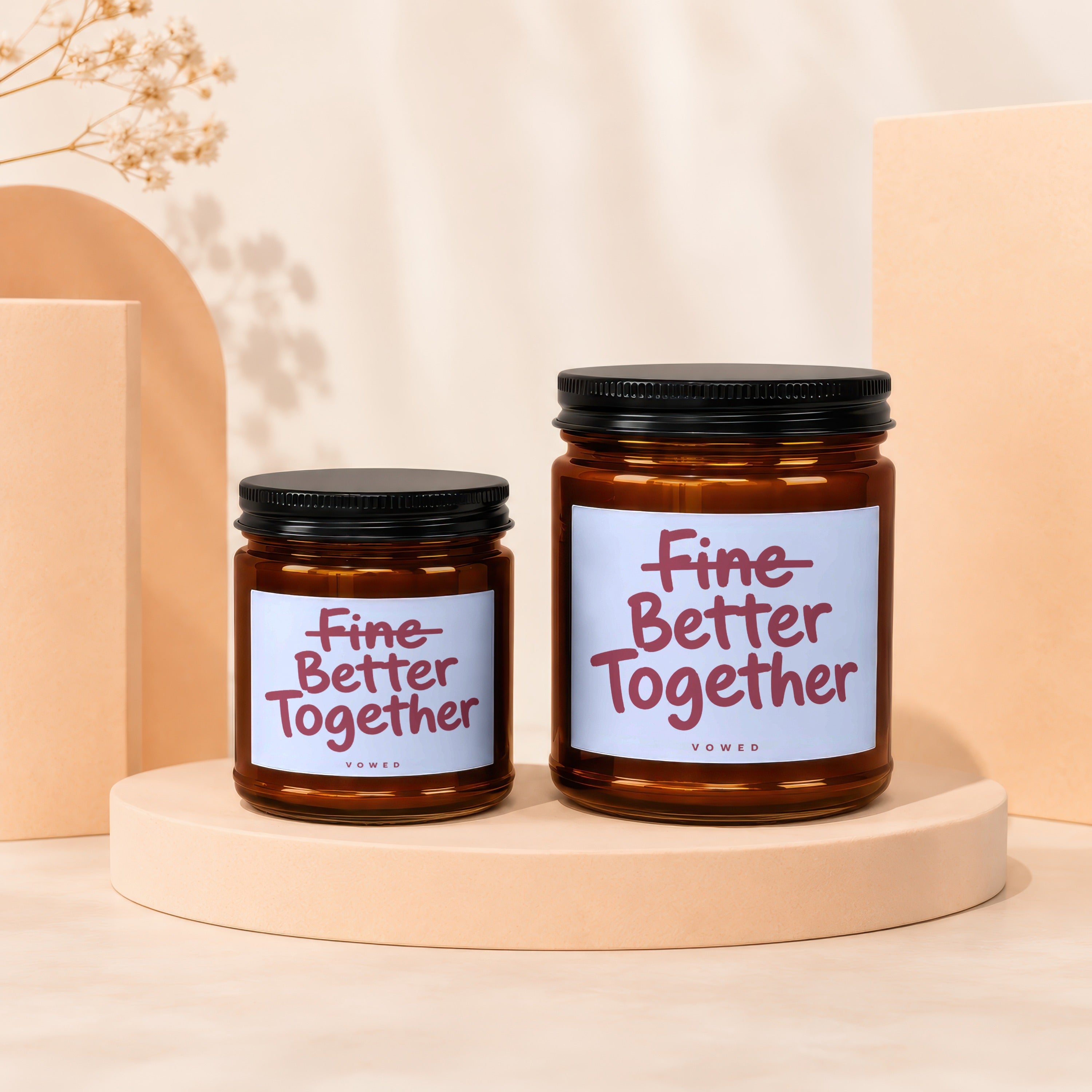 Two amber glass candles with lids, reading "Fine Better Together."