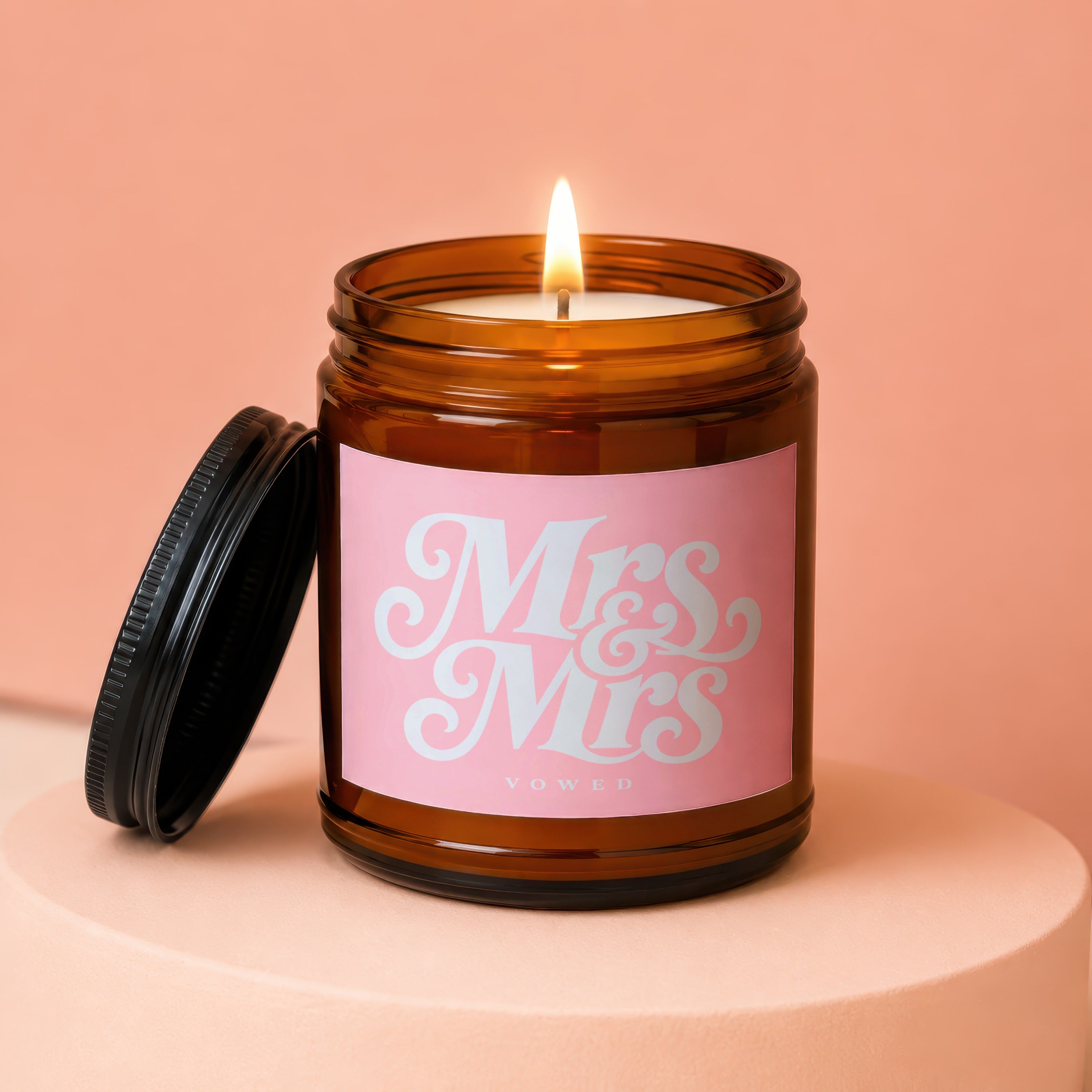 Lit amber jar candle with "Mrs & Mrs VOWED" on pink label.
