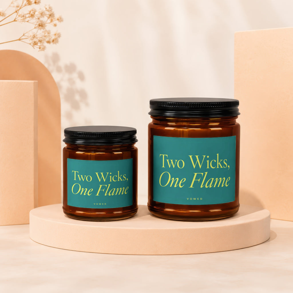 Two amber glass candles with teal labels reading "Two Wicks, One Flame."