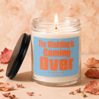 Lit candle with orange text "The Wedding Is Coming Over FINALLY VOWED" on blue label.
