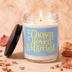 Glass candle with lit wick, blue label saying "Chosen, Loved, Married VOWED".