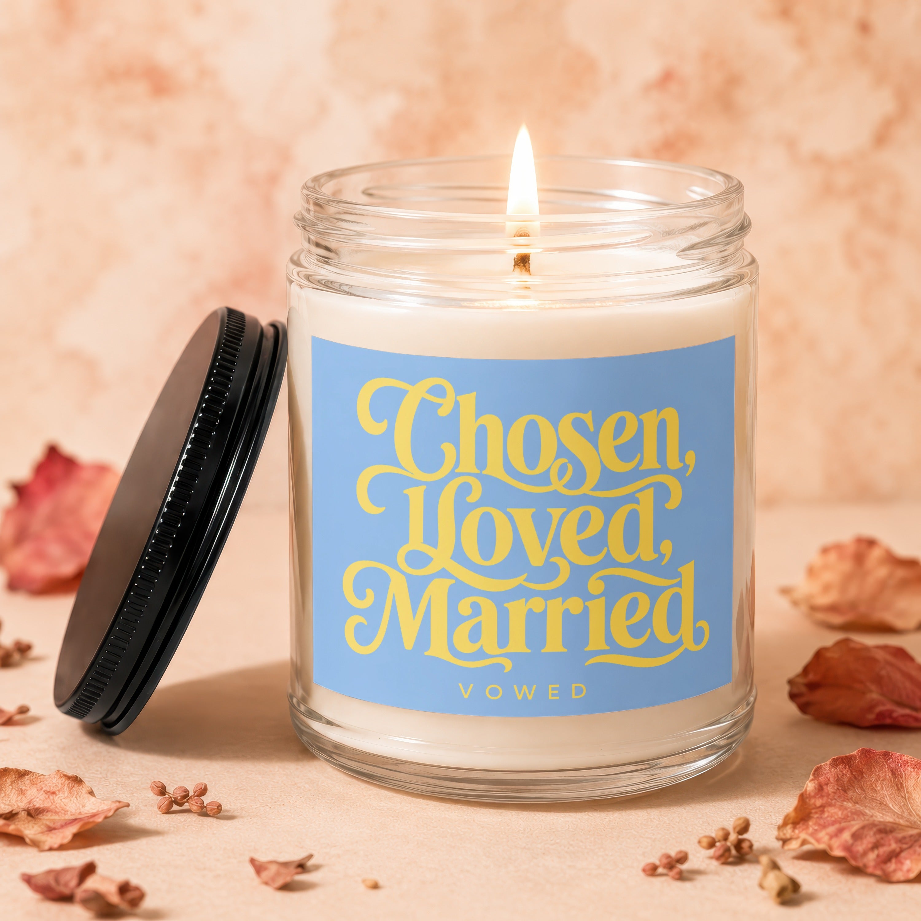 Glass candle with lit wick, blue label saying "Chosen, Loved, Married VOWED".