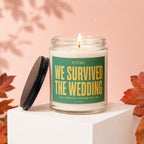 Glass candle with green label reading "STATUS: WE SURVIVED THE WEDDING ALL PARTIES ACCOUNTED FOR VOWED".