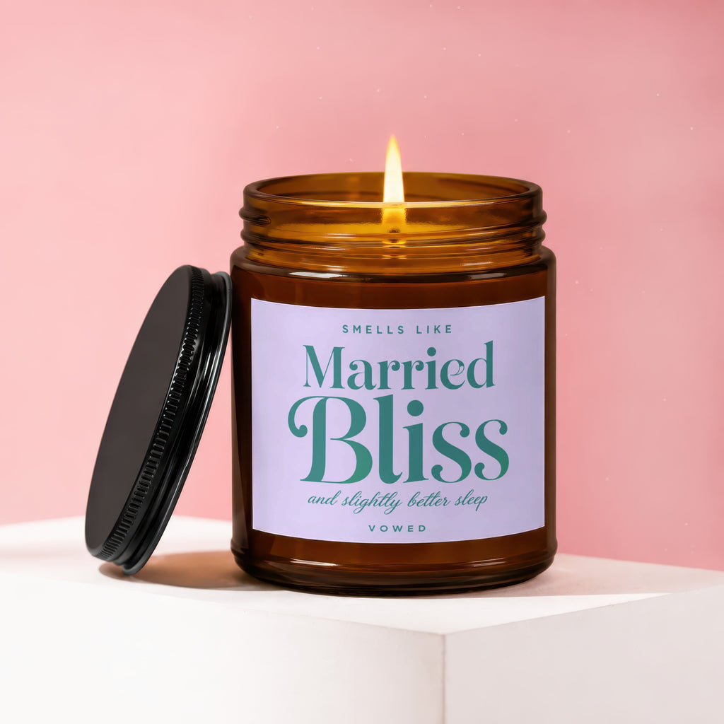 Amber jar candle with lit wick, labeled "Smells Like Married Bliss and Slightly Better Sleep".
