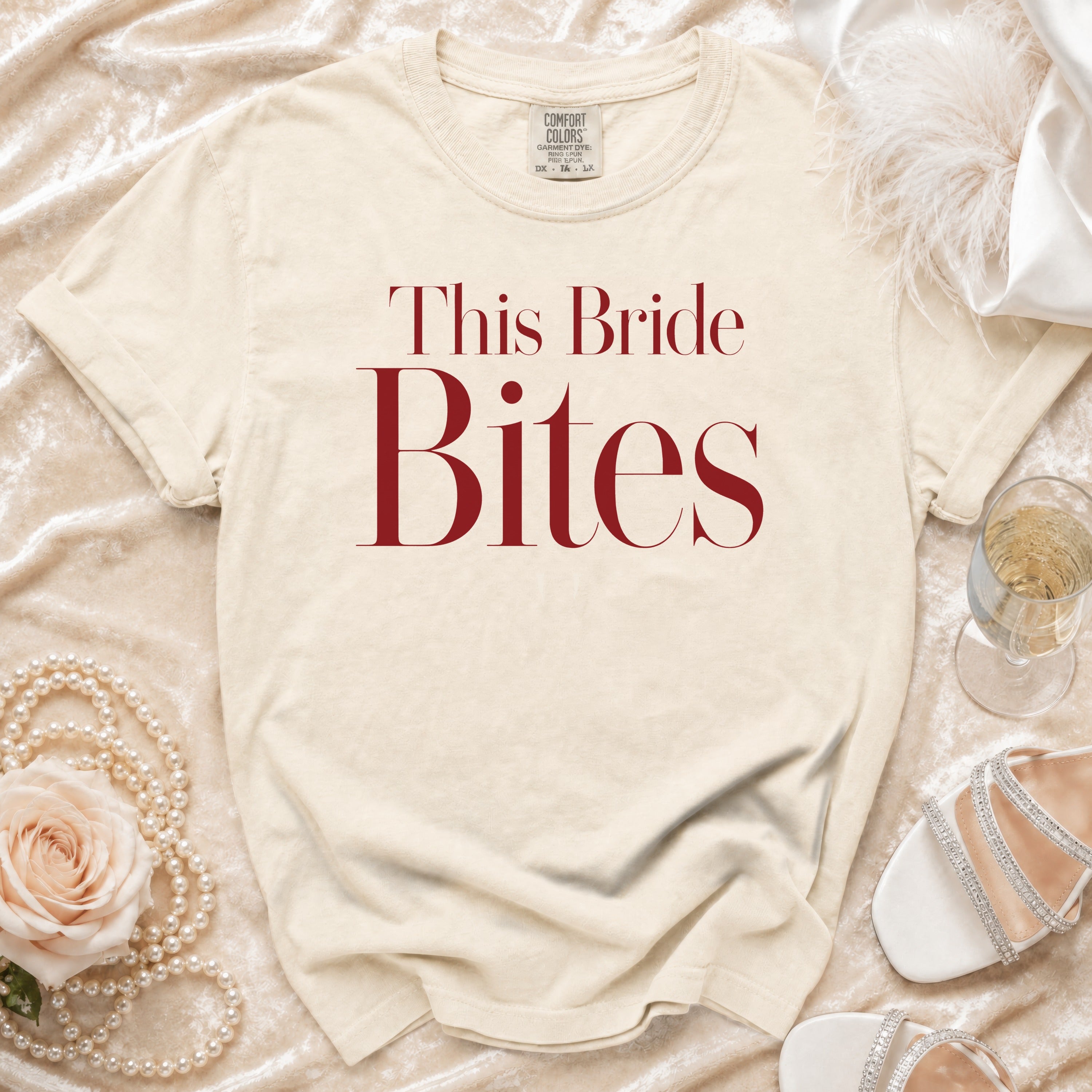 Cream t-shirt with "This Bride Bites" text in red, featuring pearl necklace and bridal shoes.