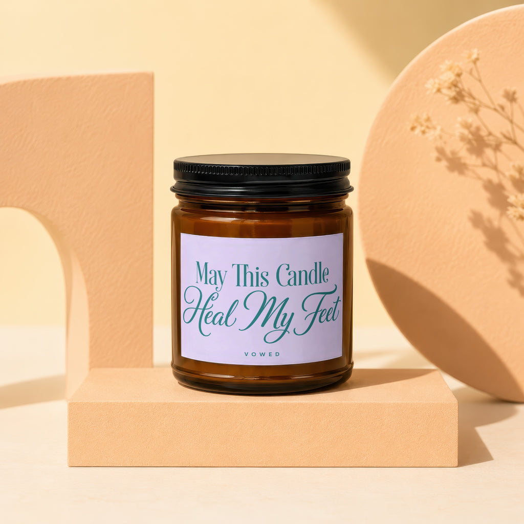 Amber glass candle with lavender label that reads "May This Candle Heal My Feet".