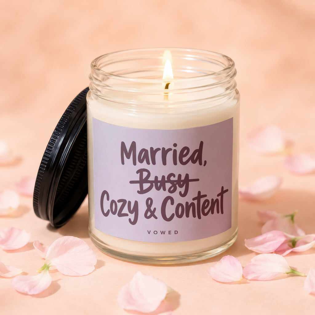 A lit candle with a label reading "Married, Busy Cozy & Content" surrounded by petals.