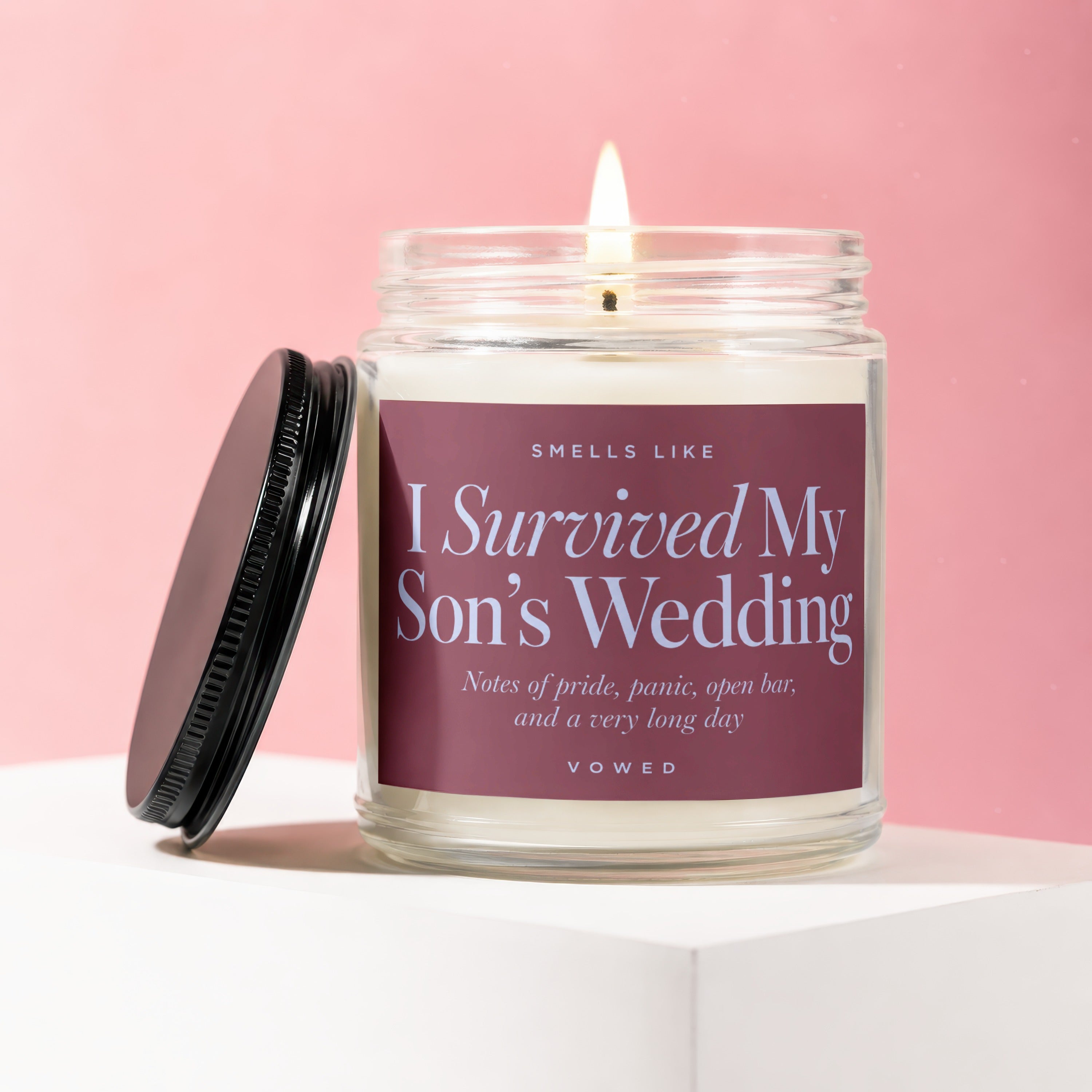 Glass candle with lit wick, reads "I Survived My Son's Wedding" and "VOWED".