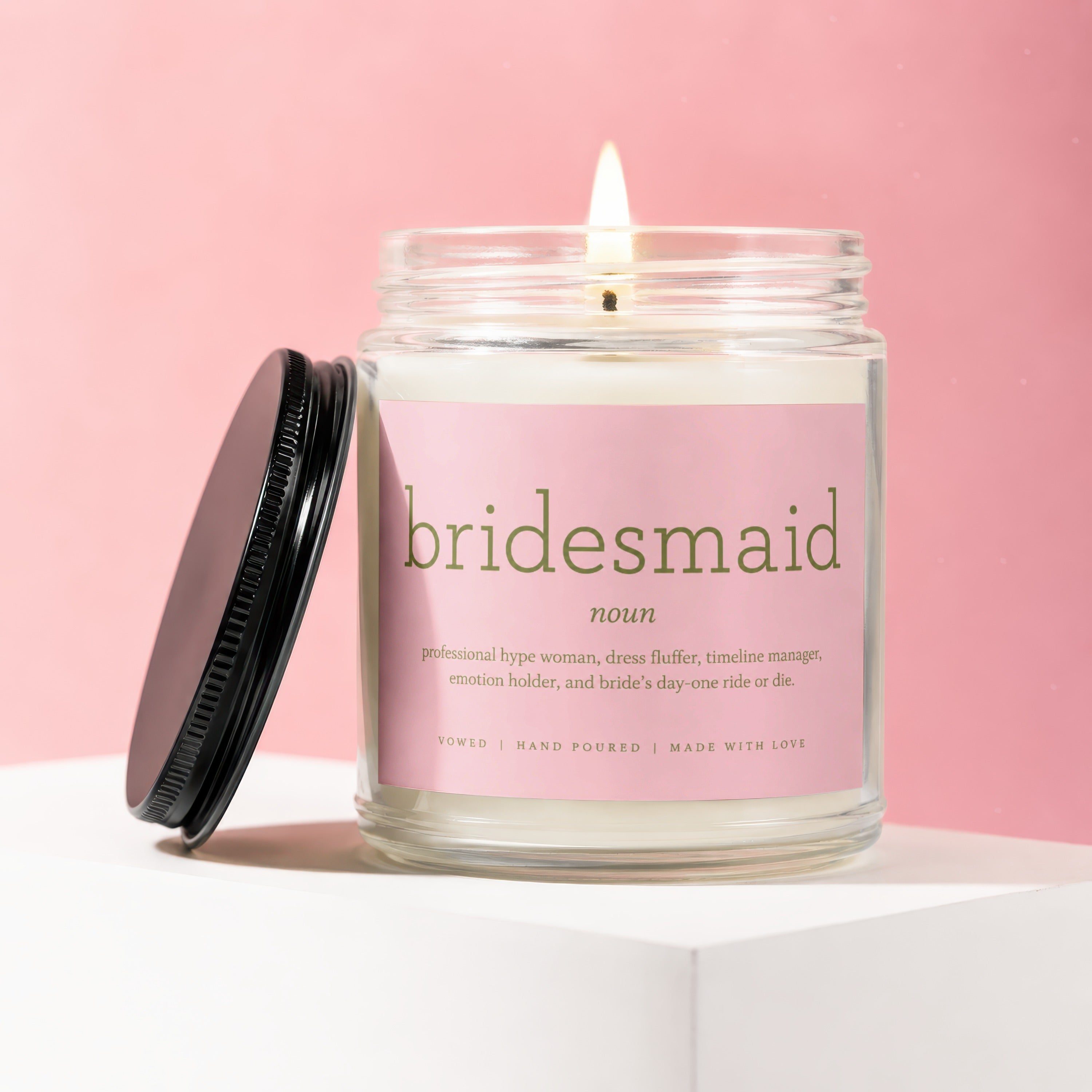 Lit candle in a jar with a pink label saying "bridesmaid noun professional hype woman, dress fluffer, timeline manager, emotion holder, and bride's day-one ride or die."
