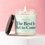 Jar candle with lit flame and black lid, reads "The Best Is Yet to Come".