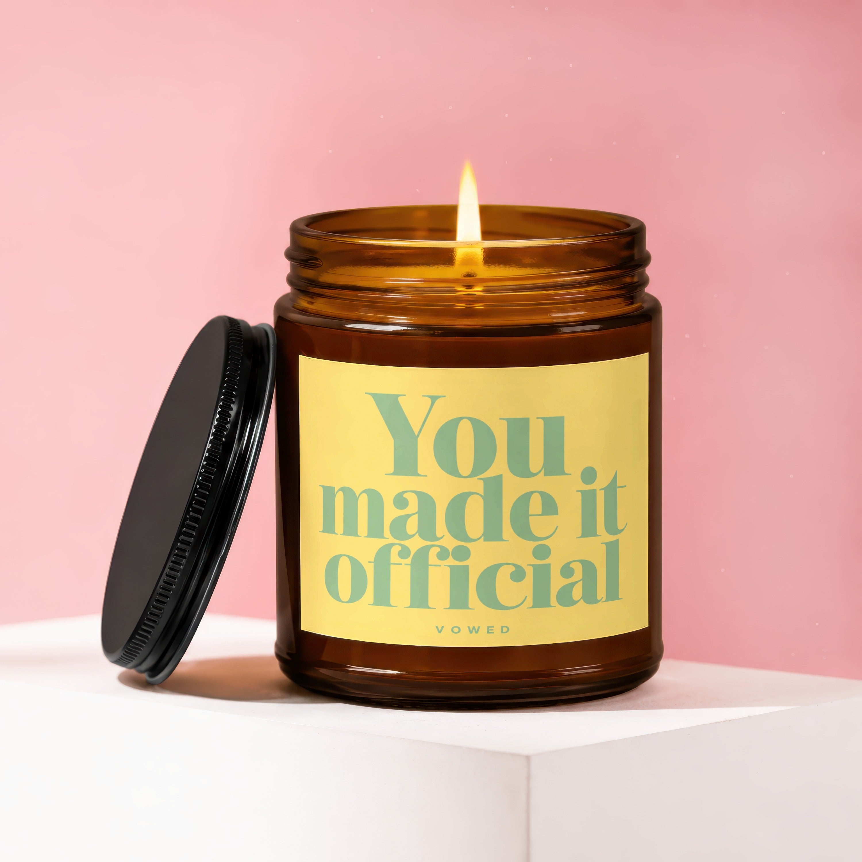 Amber jar candle with lit flame displaying "You made it official" text.
