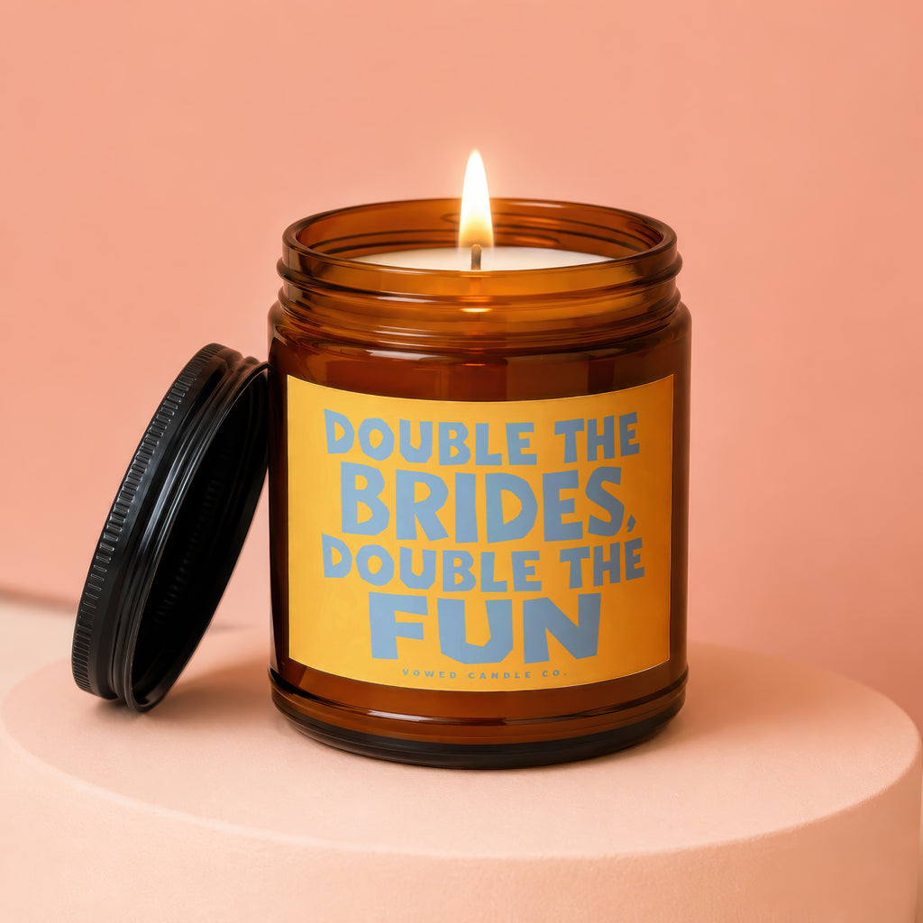 Amber jar candle with lit flame, orange label reads "Double the Brides, Double the Fun".