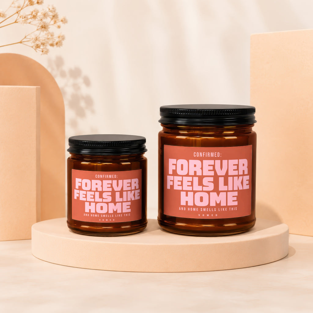 Two amber glass candles with pink labels reading "Forever Feels Like Home".