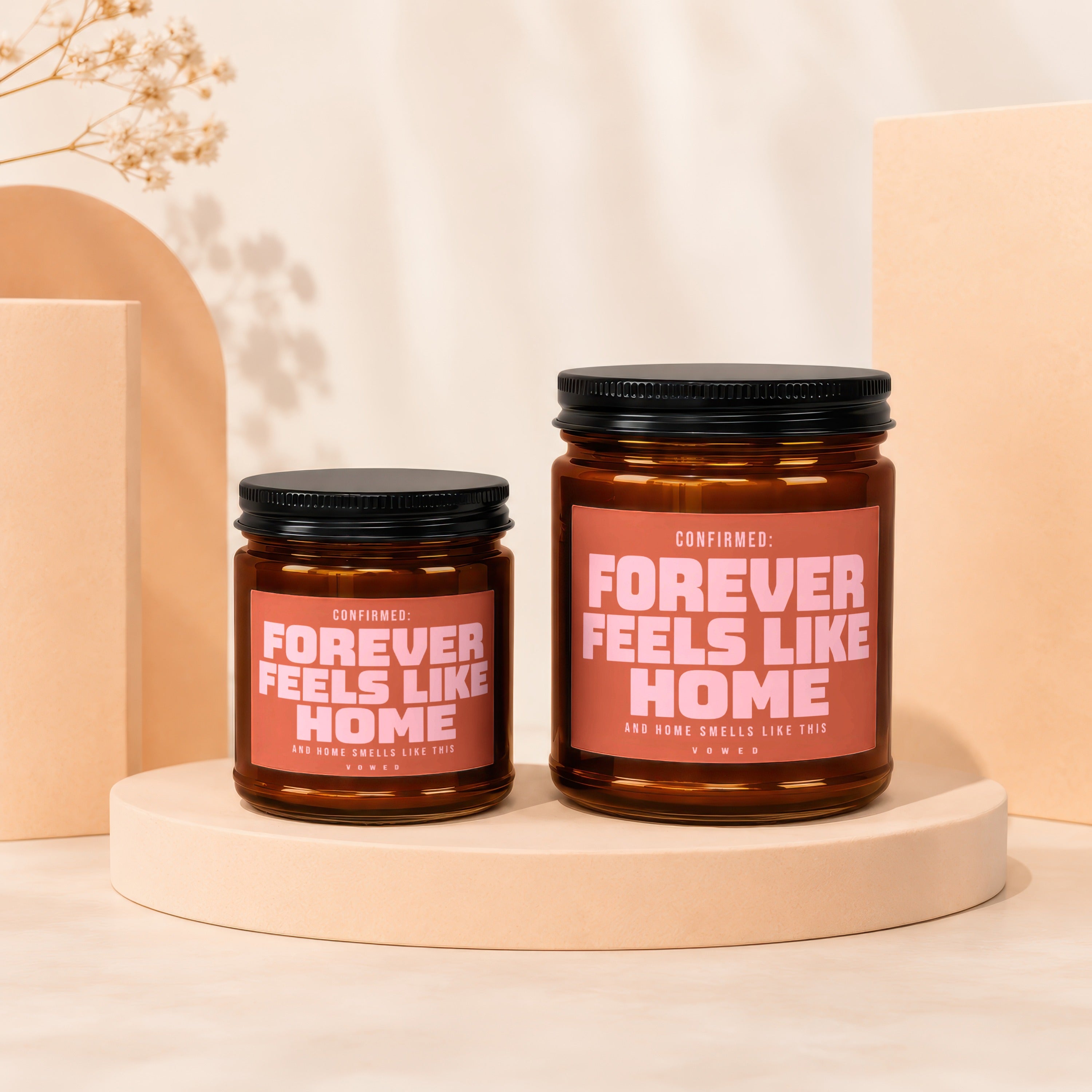 Two amber glass candles with pink labels reading "Forever Feels Like Home".