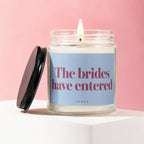 Lit candle in a jar with lid off, on a white surface against a pink background.