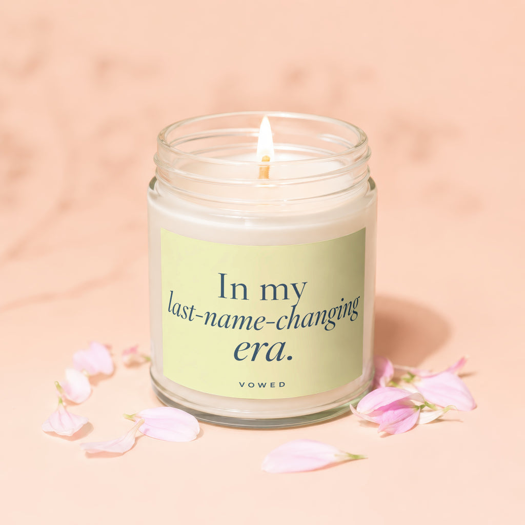 Burning candle in glass jar with "In my last-name-changing era." text and flower petals.