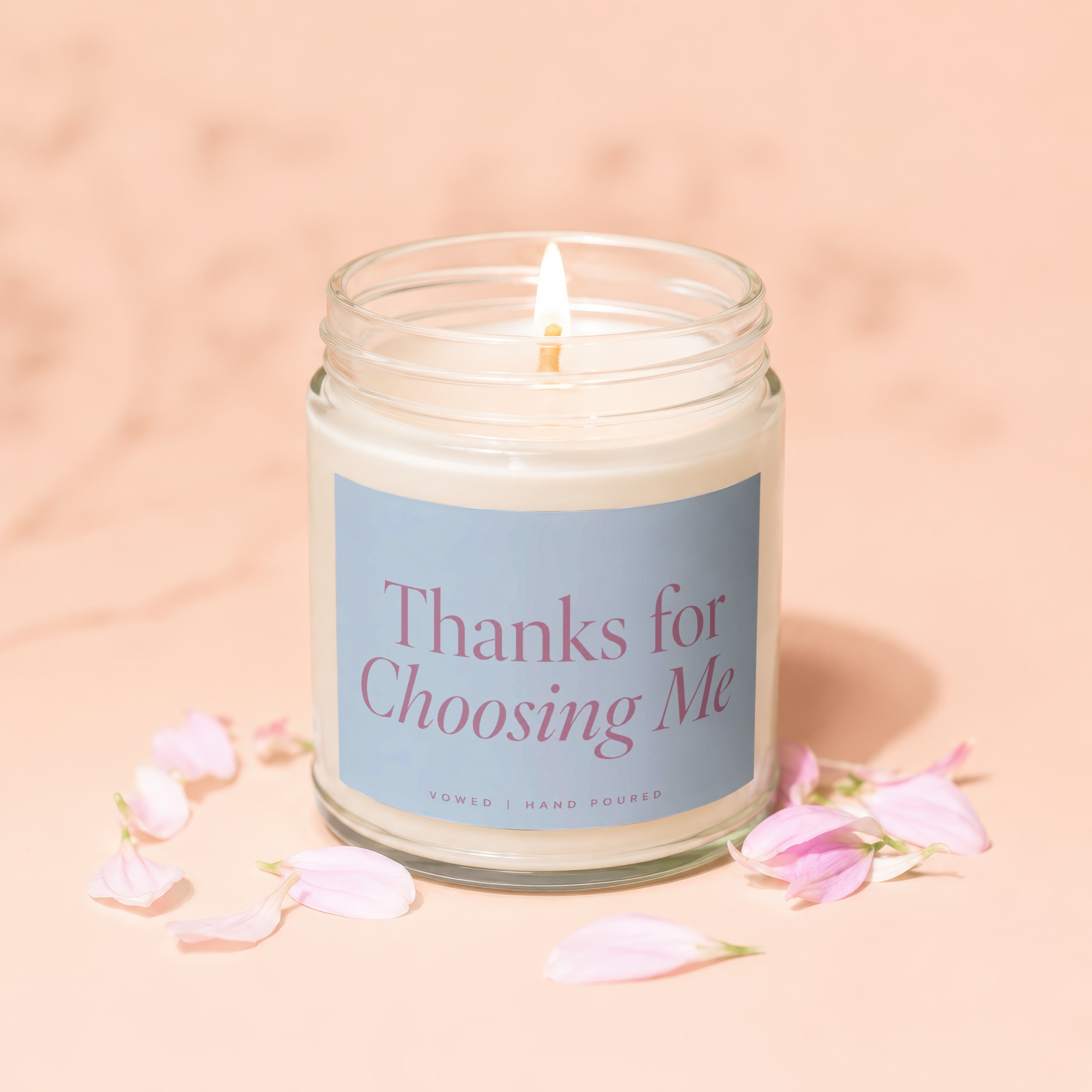Candle with lit wick on a light pink background with scattered pink petals.