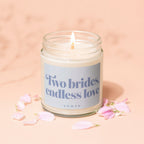Scented candle with "Two brides, endless love" text, surrounded by pink flower petals.
