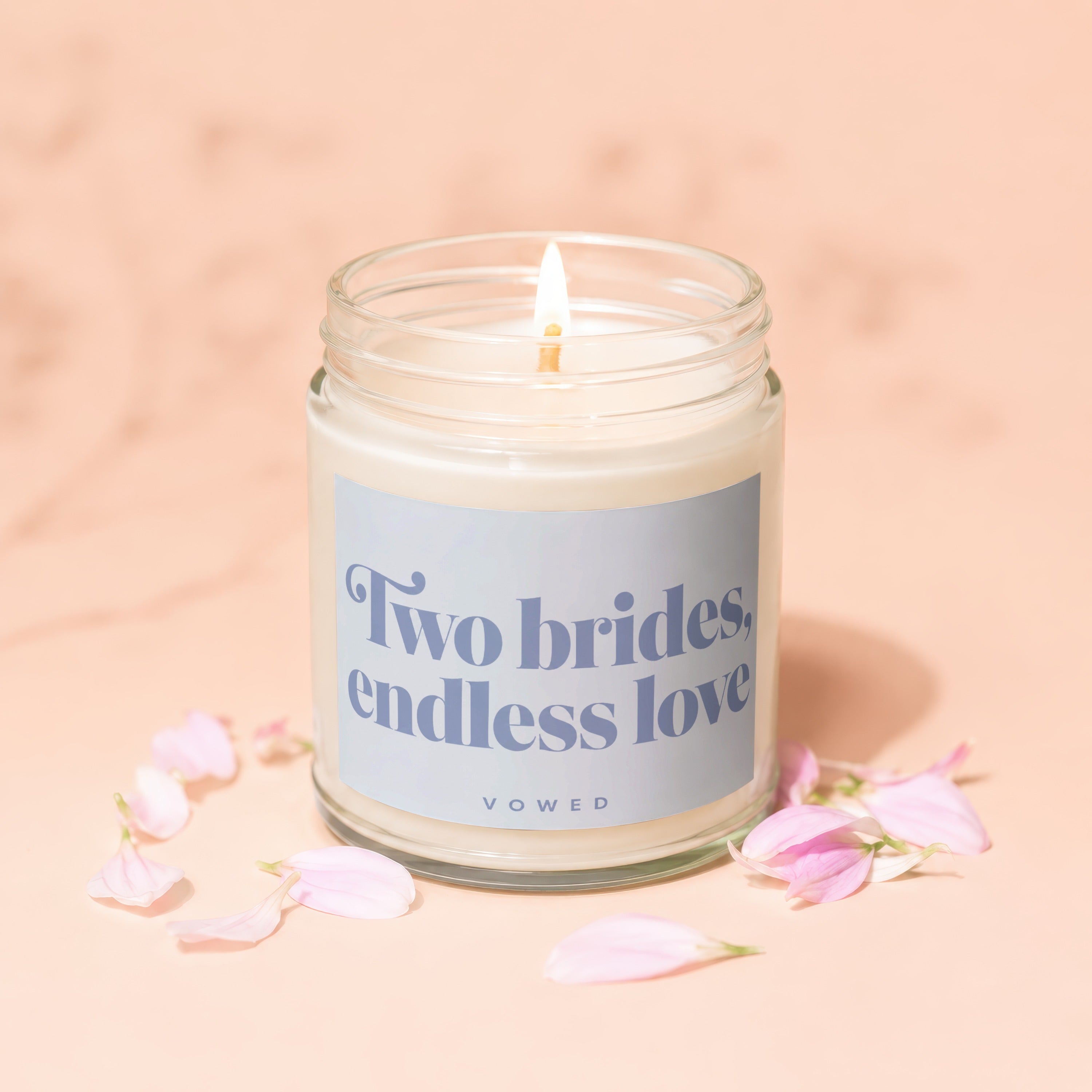 Scented candle with "Two brides, endless love" text, surrounded by pink flower petals.