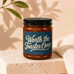 Amber jar candle with "Worth the Toaster Oven" and "VOWED" text on blue label.