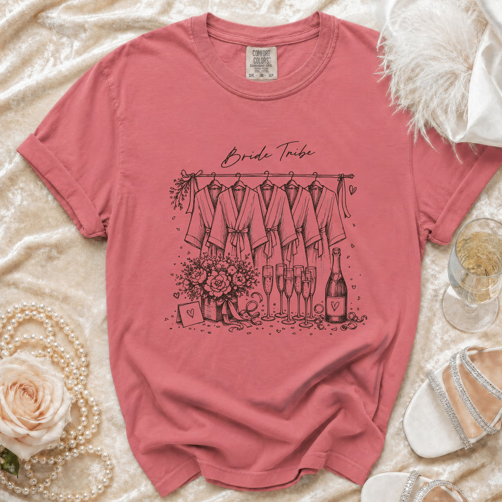 Pink t-shirt with "Bride Tribe" illustration of robes, flowers, and champagne.