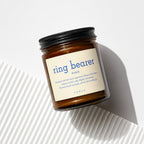 Amber glass candle with "ring bearer" definition label and black lid.