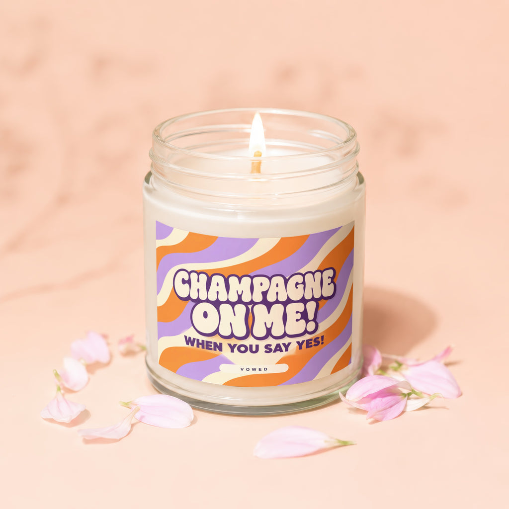 Lit candle in glass jar with "Champagne On Me! When You Say Yes!" text.
