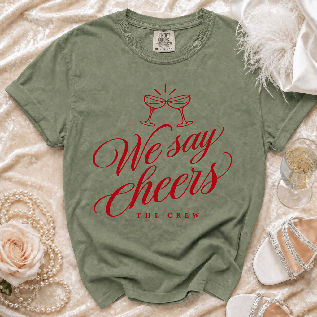 Olive green t-shirt with red "We say Cheers THE CREW" graphic and champagne glasses.