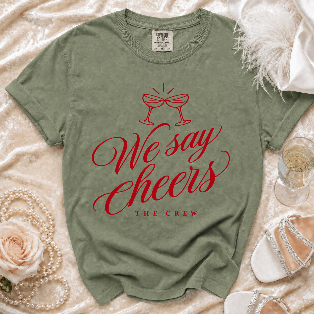 Olive green t-shirt with red "We say Cheers THE CREW" graphic and champagne glasses.