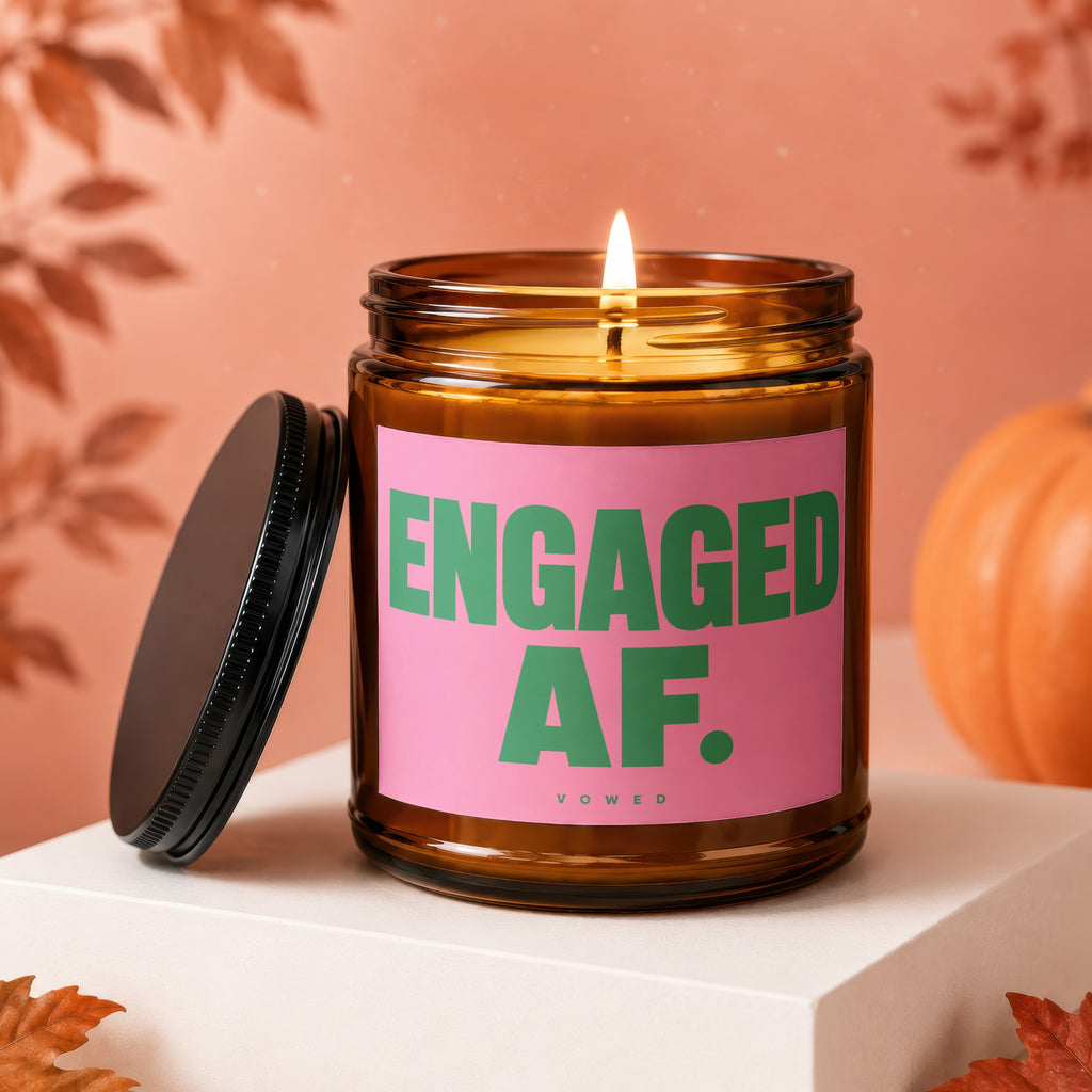 Amber candle with pink label reading "ENGAGED AF. VOWED." and a lit wick.