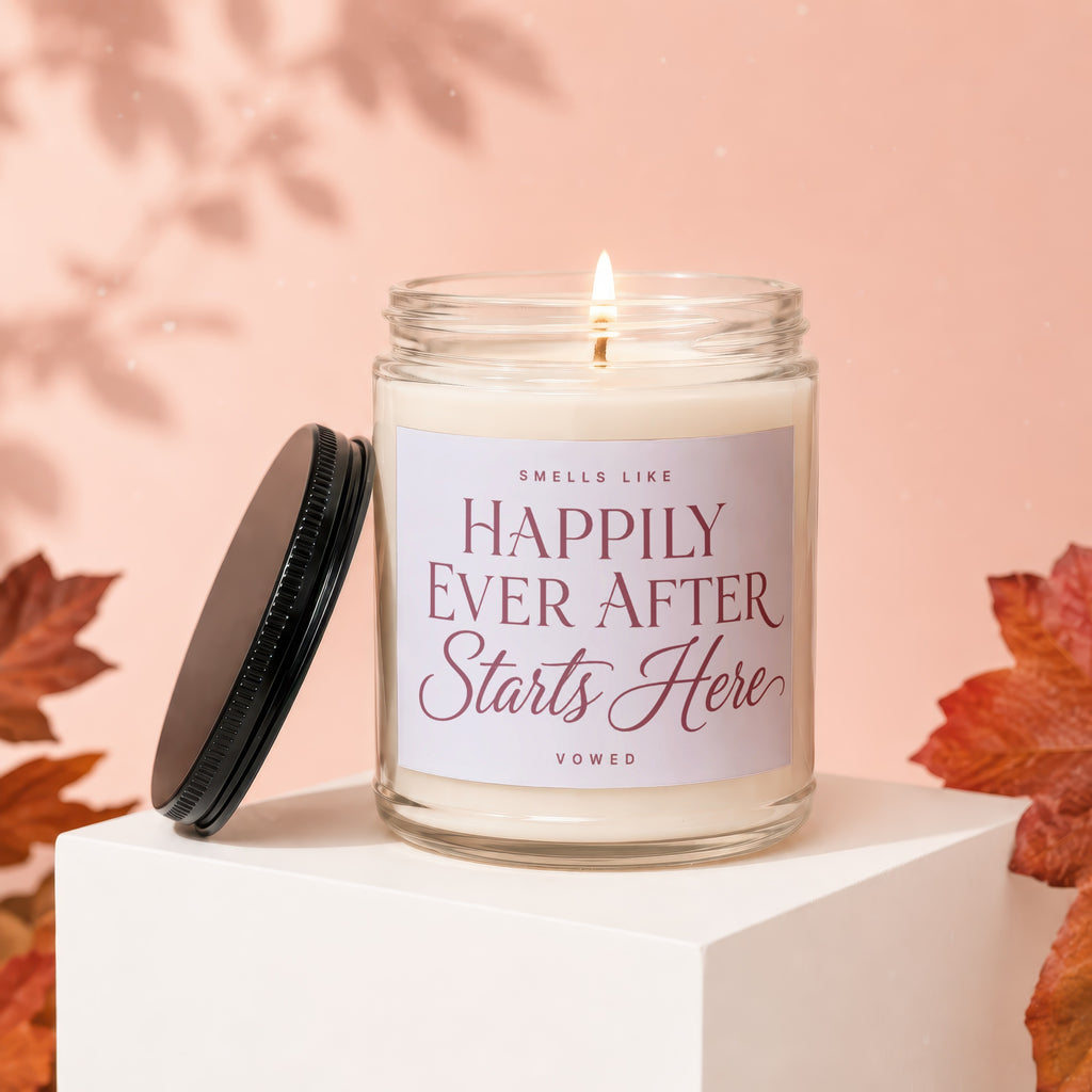Candle with lit wick, glass jar, black lid, and "Happily Ever After Starts Here" text.