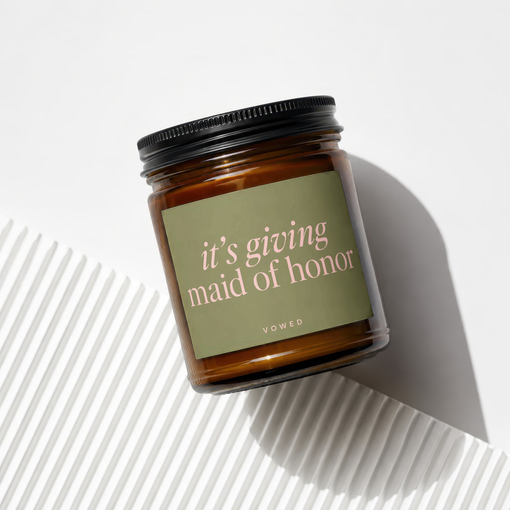 Amber glass candle with "it's giving maid of honor" text on a green label.