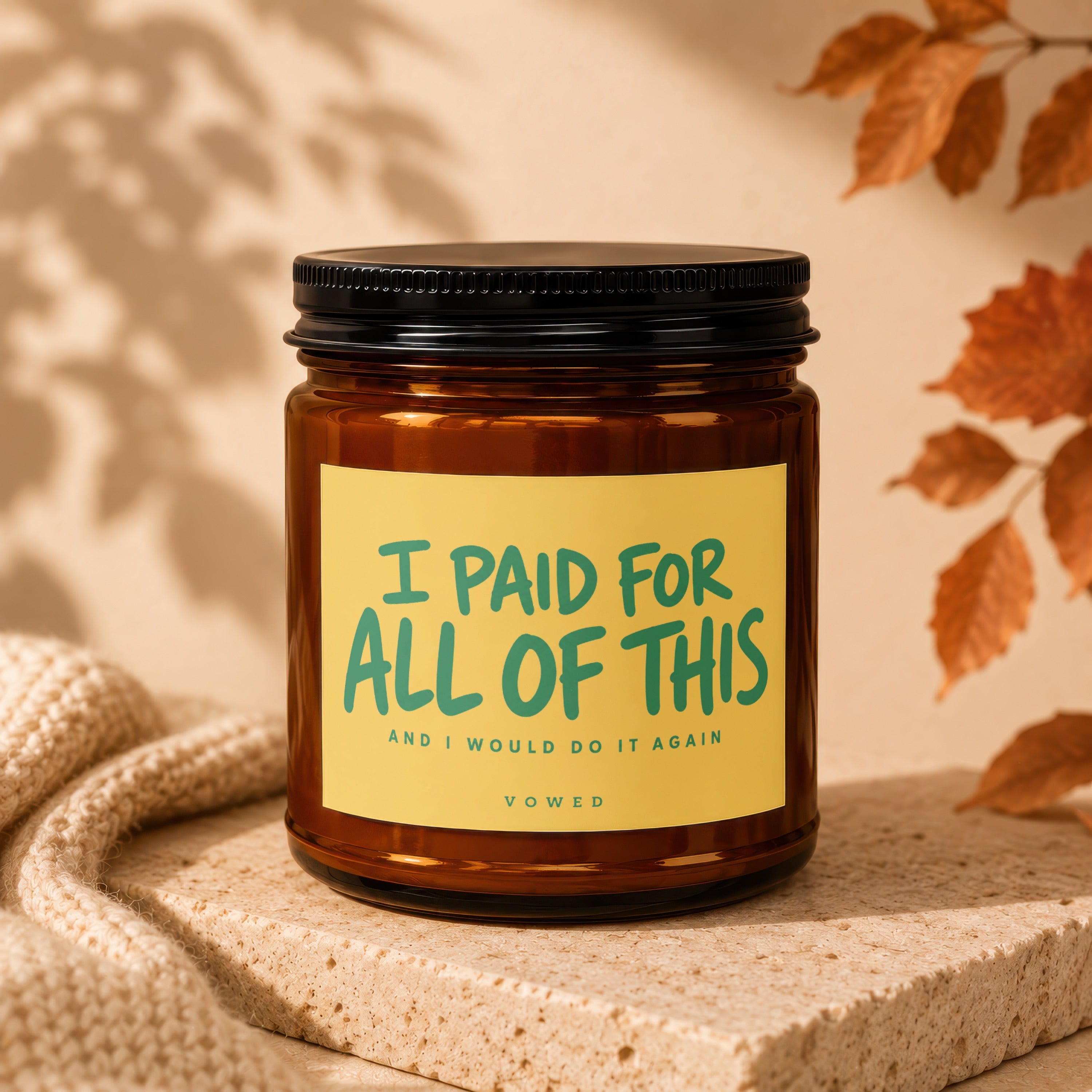 Amber glass candle with yellow label reading "I PAID FOR ALL OF THIS" and "vowed".